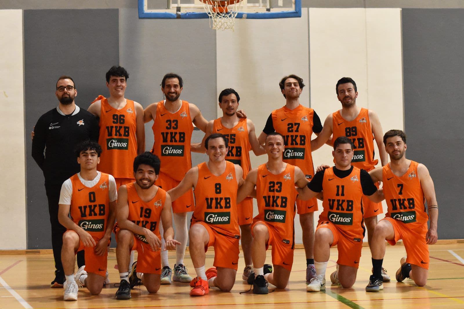El equipo sénior masculino de Vallekas Basket posa en el pabellón con la equipación naranja del club, en dos filas bajo la canasta.